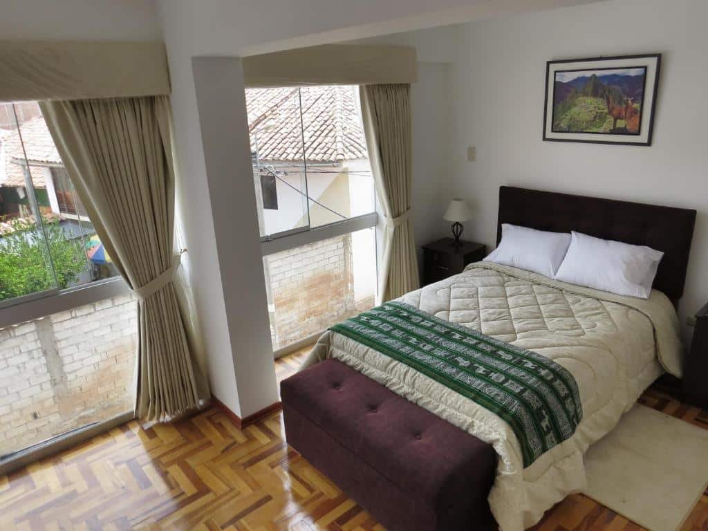 quarto do Apartamentos Quewe com uma cama de casal no lado direito e uma parede de vidro do lado esquerdo, mostrando as casas da vizinhança