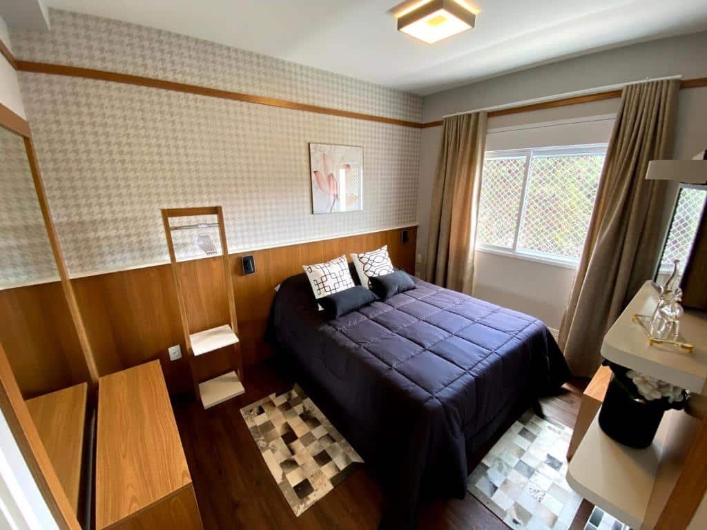 Quarto no Apartamento em Campos do Jordão ao lado do Capivari, uma cama de casal, um espelho, algumas estantes, tudo decorado, uma janela com cortinas.