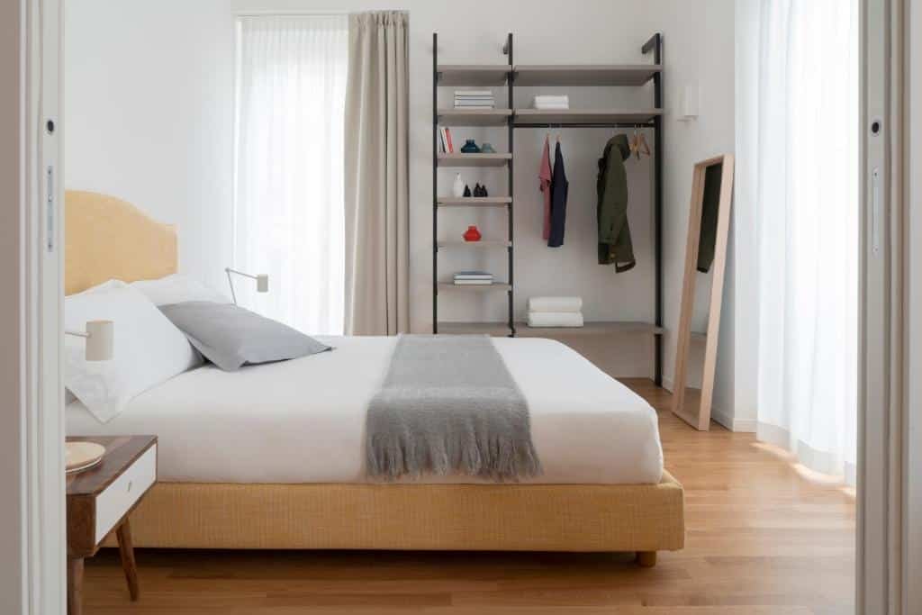 Quarto do Brera Apartments in San Babila com uma cama de casal, uma janela com cortinas, um armário de conceito aberto, chão que imita madeira e um espelho de corpo inteiro