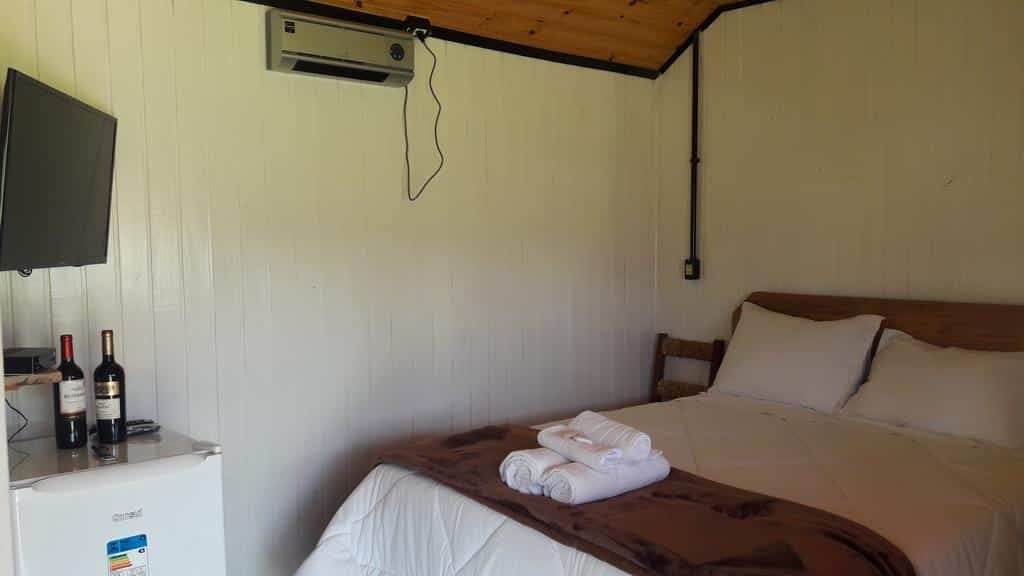 quarto das Cabanas Do Casarão Pousada Rural com uma cama de casal à direita e um pequeno frigobar e televisão à esquerda