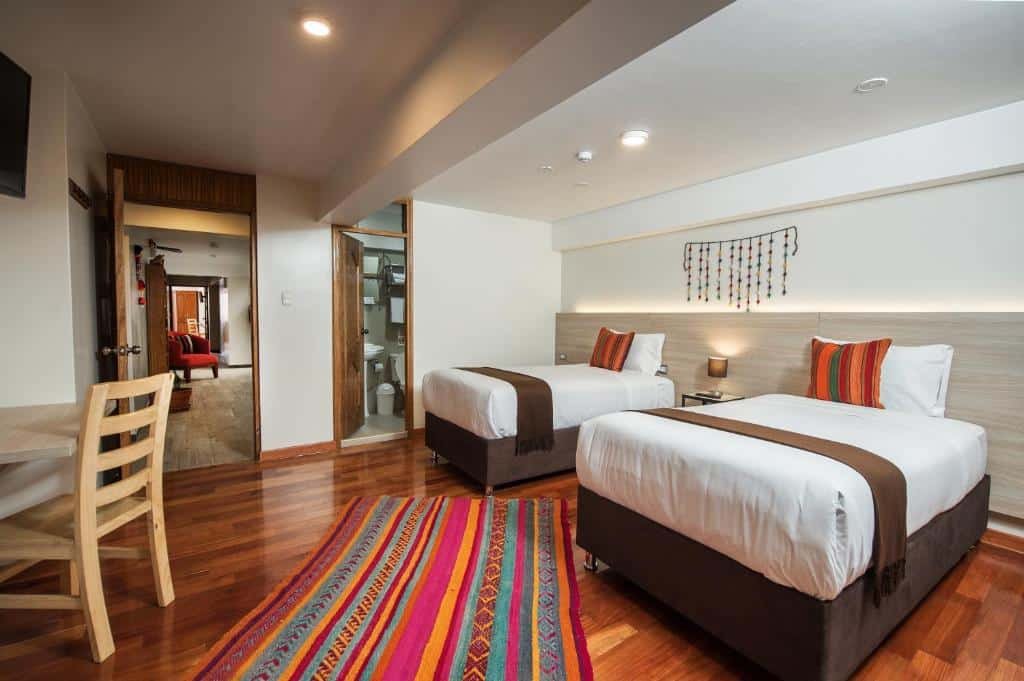 suíte do Casa Matara Boutique com duas camas de solteiro no lado direito do quarto, uma porta com vista para o banheiro no centro da imagem, e uma mesa com cadeira de madeira dispostas em frente as camas, no lado esquerdo.
