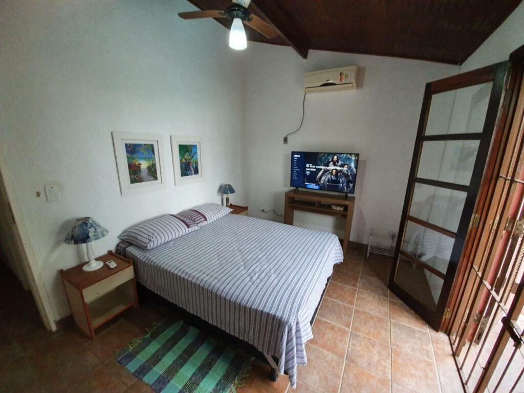 Quarto da Casa pé na areia em Toque Toque com cama de casal do lado esquerdo da imagem com uma cômoda em cada lado da cama com luminária. Representa airbnb em Toque-Toque Grande.