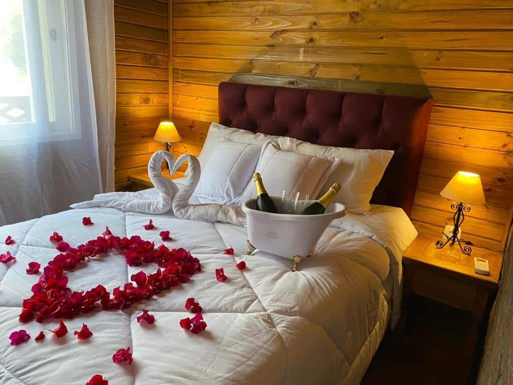 Quarto do Chales e Spa Exclusive – Localizado Proximo do Centro com cama de casal, com duas cômodas de madeira ao lado com duas luminárias, rosas em cima da cama com um balde de champanhe em cima da cama.