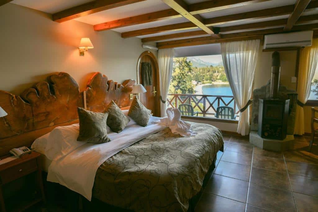 Quarto do Charming Luxury Lodge & Private Spa com cama apla, duas cômodas com luminária do lado esquerdo janela ampla com cortinas brancas com vista para um lago e uma pequena lareira do lado esquerdo.