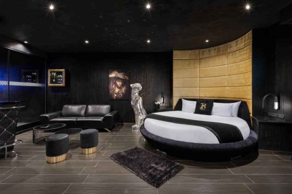 Quarto amplo no H Hotel & SPA - Adults Only em tons de preto e cinza, uma cama redonda, um tapete pequeno, uma sofá de couros preto e alguns itens de decoração, para representar hotéis em Malta