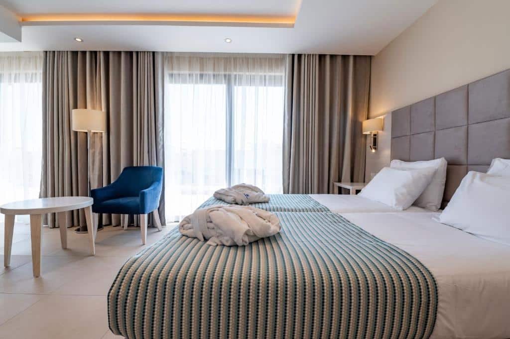 Quarto do Maritim Antonine Hotel & Spa, com uma varanda, duas camas de solteiro, uma mesinha de centro, uma poltrona e um abajur de chão, tudo em tons de cinza, azul e branco