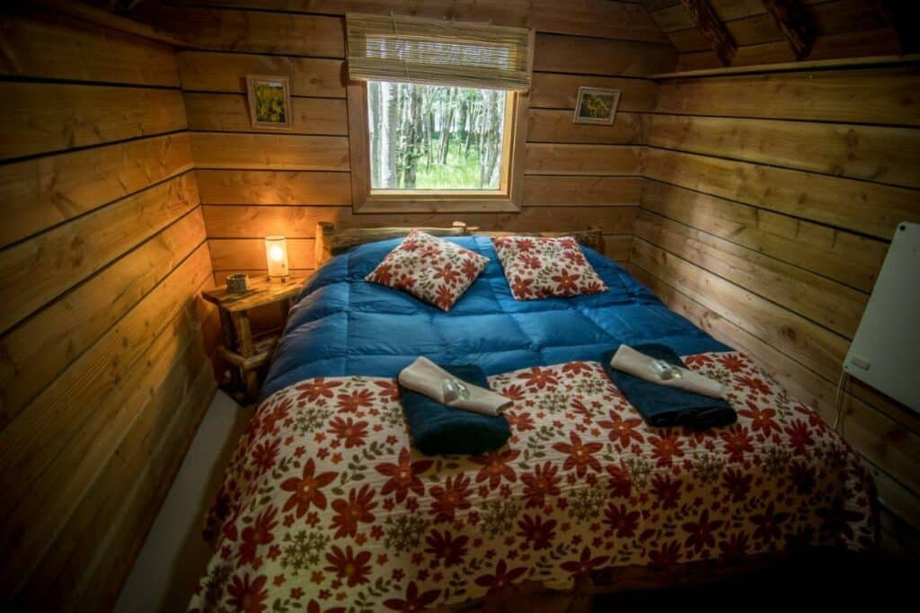 Quarto do Laguna Condor – Refugio de Montaña com uma cama de casal no centro com uma cômoda do lado esquerdo da imagem. Representa hotéis em El Chalten.