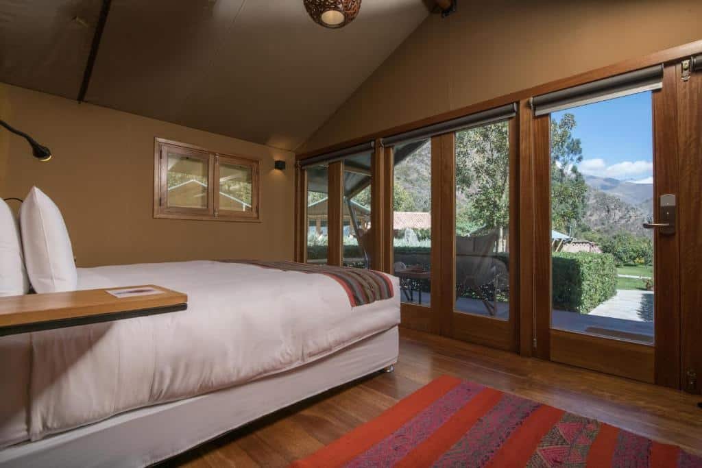tenda da suíte do Las Qolqas EcoResort Ollantaytambo, para representar o post onde ficar em machu picchu, com uma cama de casal à esquerda com vista para as portas de vidro que dão acesso a varanda aberta e visão para a natureza e montanhas da região