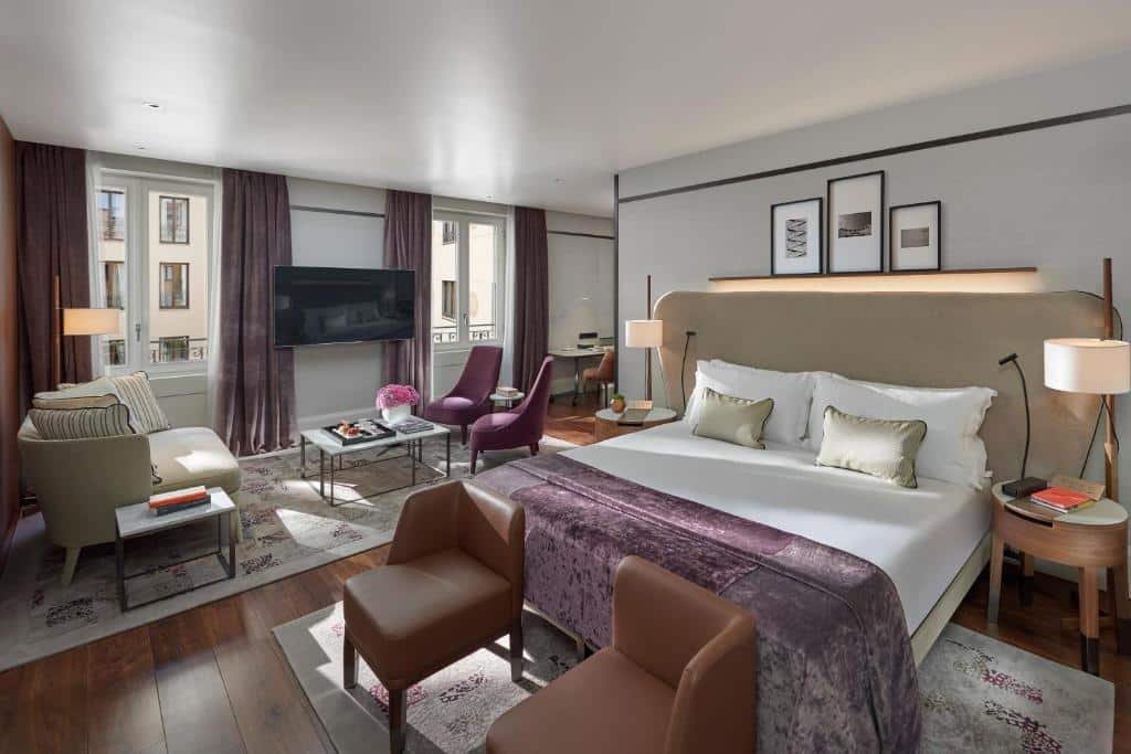 Quarto grande no Mandarin Oriental, Milan com uma cama de casal, duas janelas com cortinas, há duas poltronas no pé da cama, mais próximo das janelas, há um sofá, uma televisão, uma mesa de centro, duas poltronas e um tapete, para representar os melhores hotéis em Milão