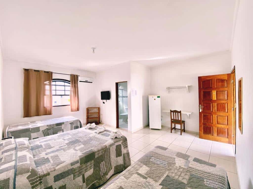 Quarto em Pousada Beija Flor Praia Grande, três camas de solteiro, um banheiro, uma janela ampla, uma geladeira, um televisão, uma cadeira e duas prateleiras