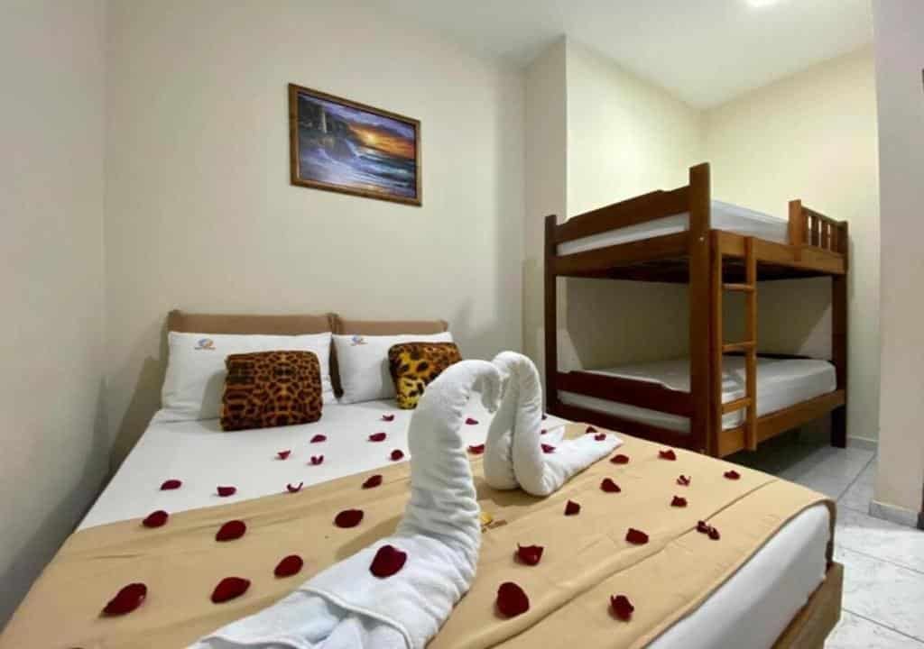 Quarto da Pousada Mar Suites, uma cama de casal e uma beliche, sob a cama de casal tem duas toalhas, pétalas de rosas e travesseiros