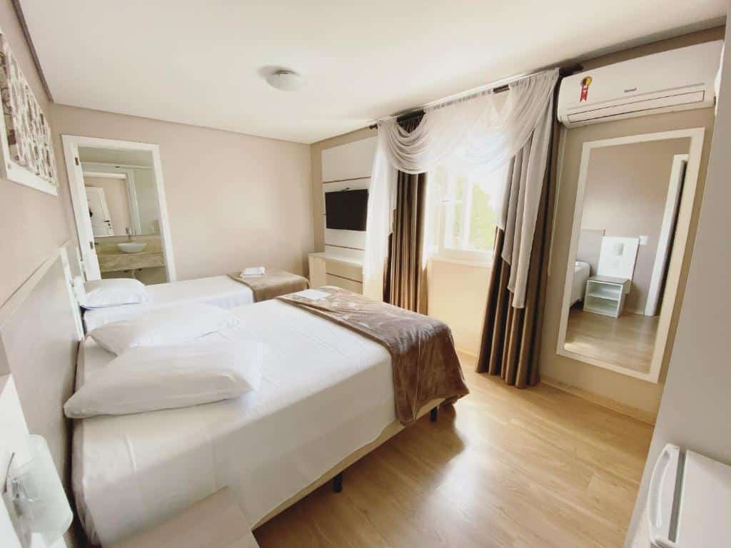 quarto da Pousada Vovô Nino com uma cama de casal e uma de solteiro no canto esquerdo, e um espelho vertical no canto direito. Ao fundo é possível ver uma porta aberta com acesso ao banheiro.
