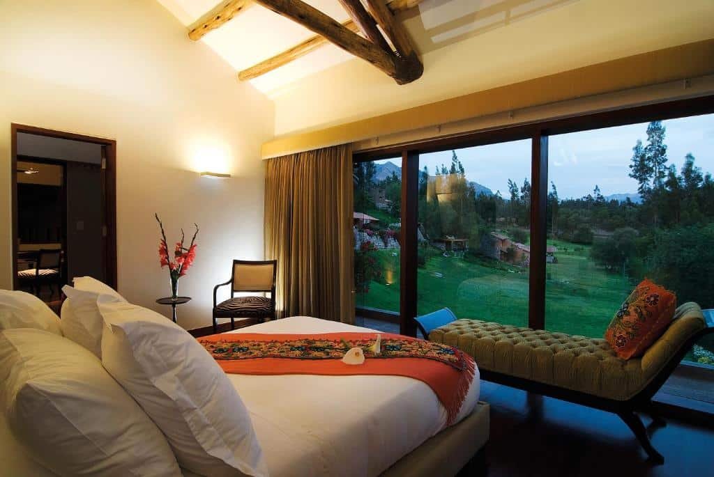 suíte do Rio Sagrado, A Belmond Hotel, Sacred Valley com uma cama de casal disposta em frente às paredes de vidro que dão visão a paisagem panorâmica do Vale Sagrado dos Incas