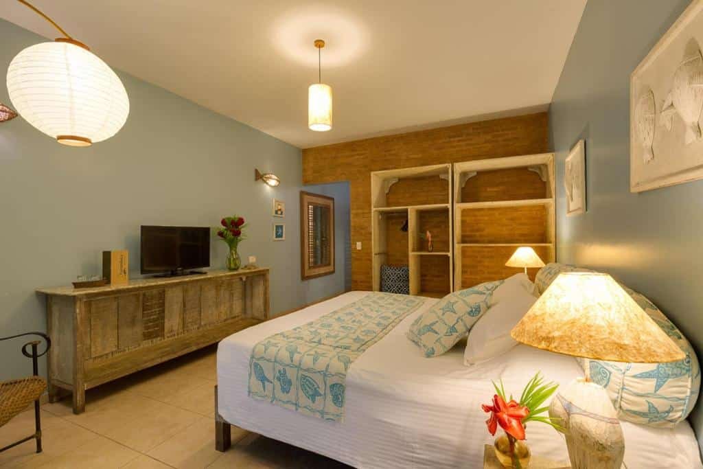 Quarto no Itamambuca Eco Resort com uma cama de casal, um armário de conceito aberto, duas luminárias rústicos no teto, um móvel também rústico em estilo de cômoda com uma televisão em cima. Representa airbnb na praia da Lagoinha.