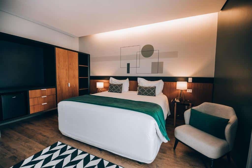 Quarto da Villa Amistà Campos do Jordão com uma cama de casal, poltrona, tapete preto e branco, um armário de madeira com estilo conceito aberto, alguns itens de decoração e dois abajures