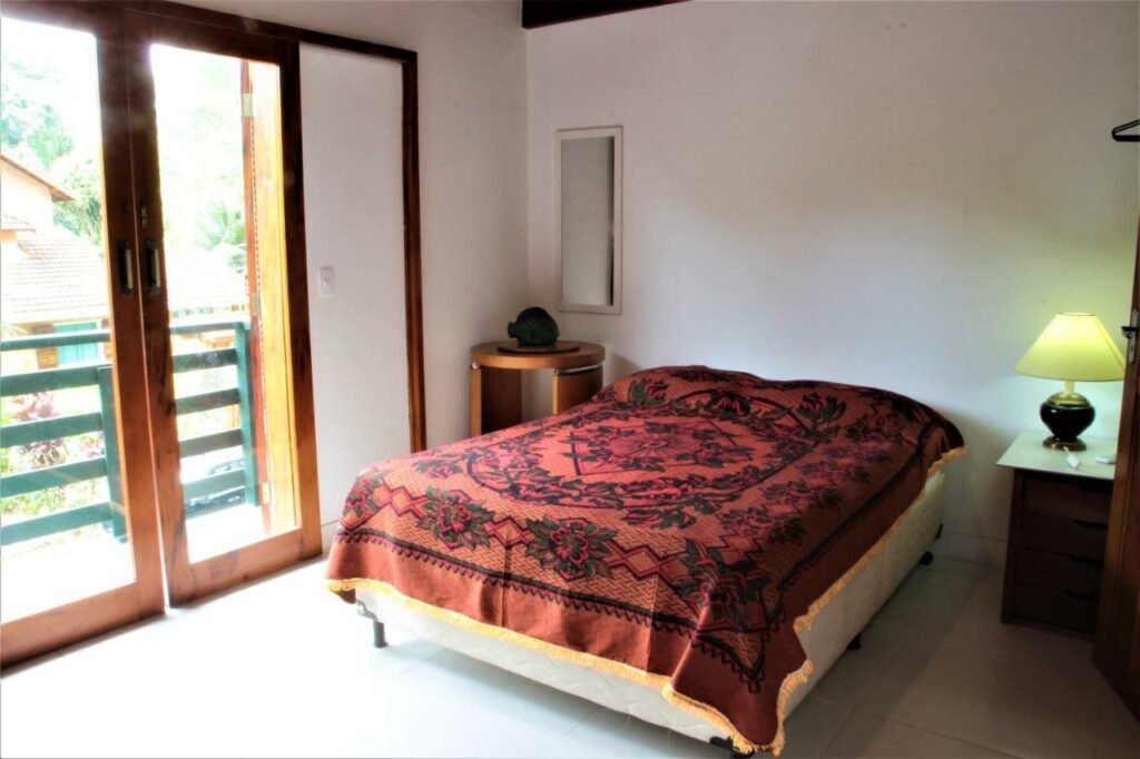 Quarto da Villa Félix Suites e Chalés  com cama de casal no centro do quarto com uma cômoda do lado esquerdo com luminária e do lado direito uma cômoda.