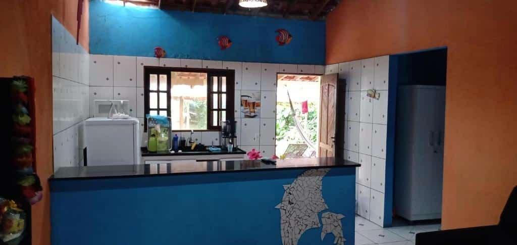 Cozinha do Rancho valhalla ubatumirim. Uma bancada na frente, no fundo uma geladeira, uma pia, a porta e uma janela.