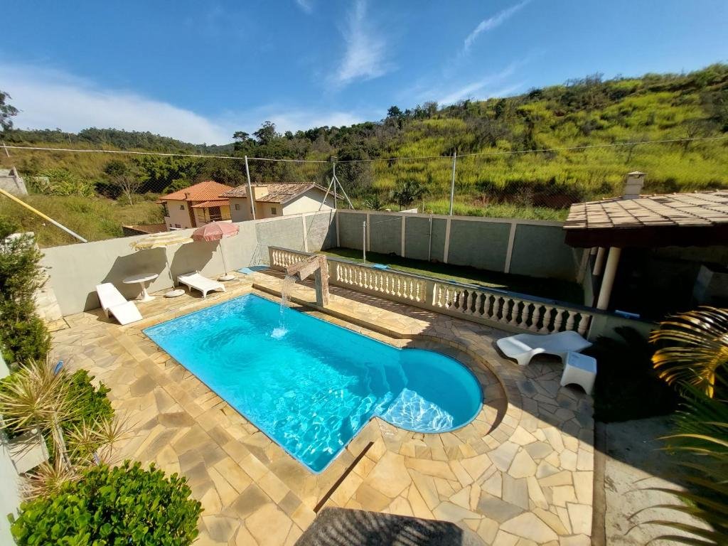 Vista aérea de Recanto Serra Negra - Sossego e lazer! Há um deck de pedra com uma piscina. Há algumas espreguiçadeiras com guarda-sol. A vista no fundo é pra a vegetação.