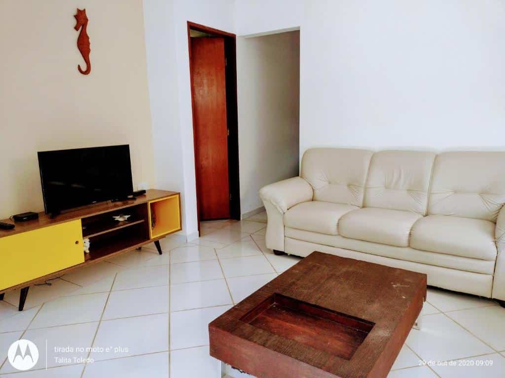 Sala e estar do Recanto Canoa Pequena. Um sofá do lado direito, no centro uma mesa de madeira. Do lado esquerdo uma raque com uma televisão.