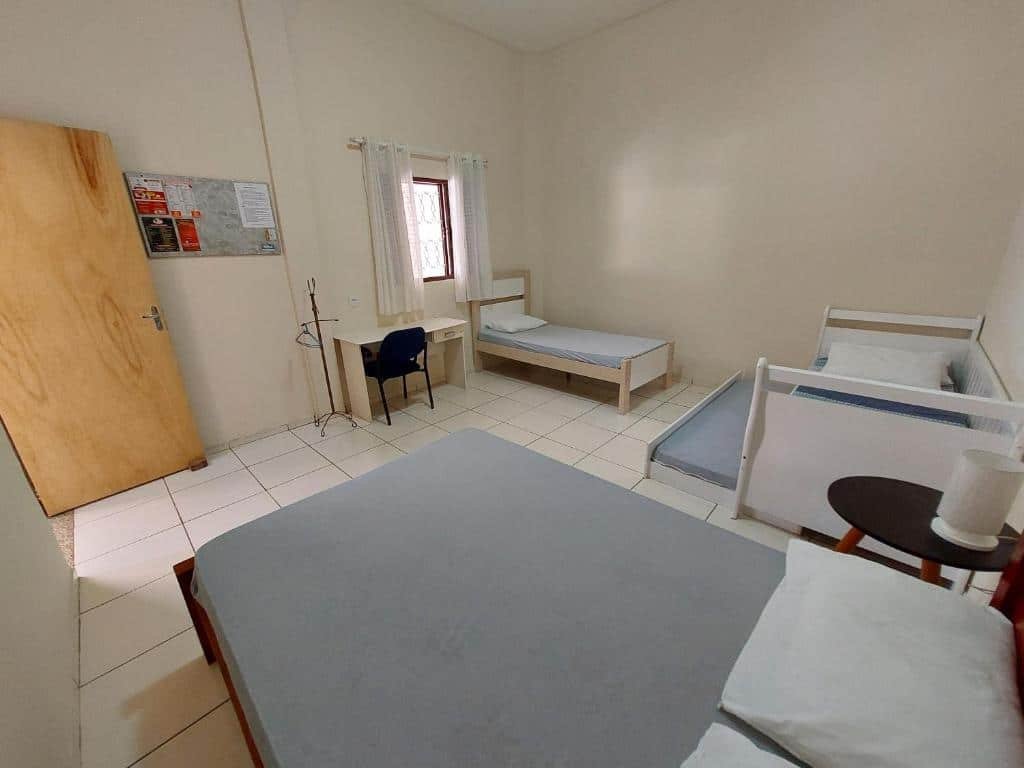 Foto do quarto em Recanto Serra Negra - Sossego e lazer! A cama de casal está no canto inferior da foto, ao lado dela, na direita, há três camas para crianças. Do lado da cama no fundo à direita há uma mesa com cadeira. A porta do quarto está na esquerda, de frente para a cama de casal.
Ilustra o post sobre airbnb em Serra Negra.