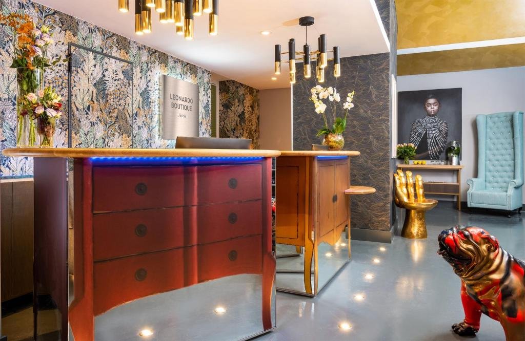 recepção do Leonardo Boutique Hotel Rome Termini, com bancadas que imitam cômodas, lustres com cilindros, poltrona em forma de mão e outra com encosto alto, em um ambiente bem conceitual