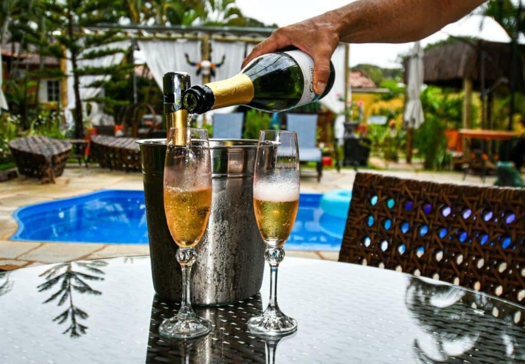 Área da piscina da Pousada Relais Amadeus Pousada de Charme, em primeiro plano duas taças e um champagne sendo servido. 