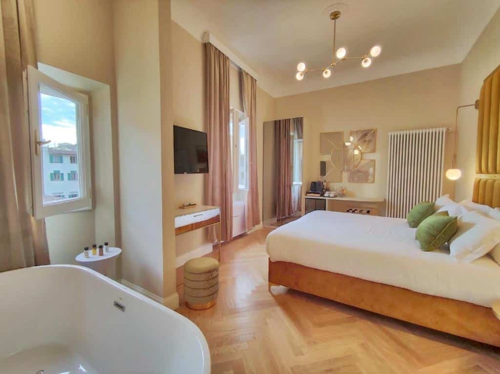 Quarto deluxe do Renascentia Garden Relais de 28 m², com hidromassagem, cama de casal com travesseiros e almofadas em cima, TV, espelho grande e mesinha com itens para fazer chá ou café