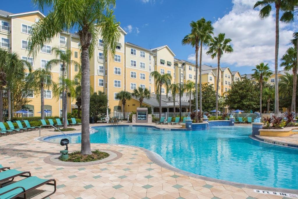 piscina de bordas sinuosas que avança pela área comum do Residence Inn by Marriott Orlando, um dos hotéis em Orlando, com palmeiras e espreguiçadeiras espalhadas 