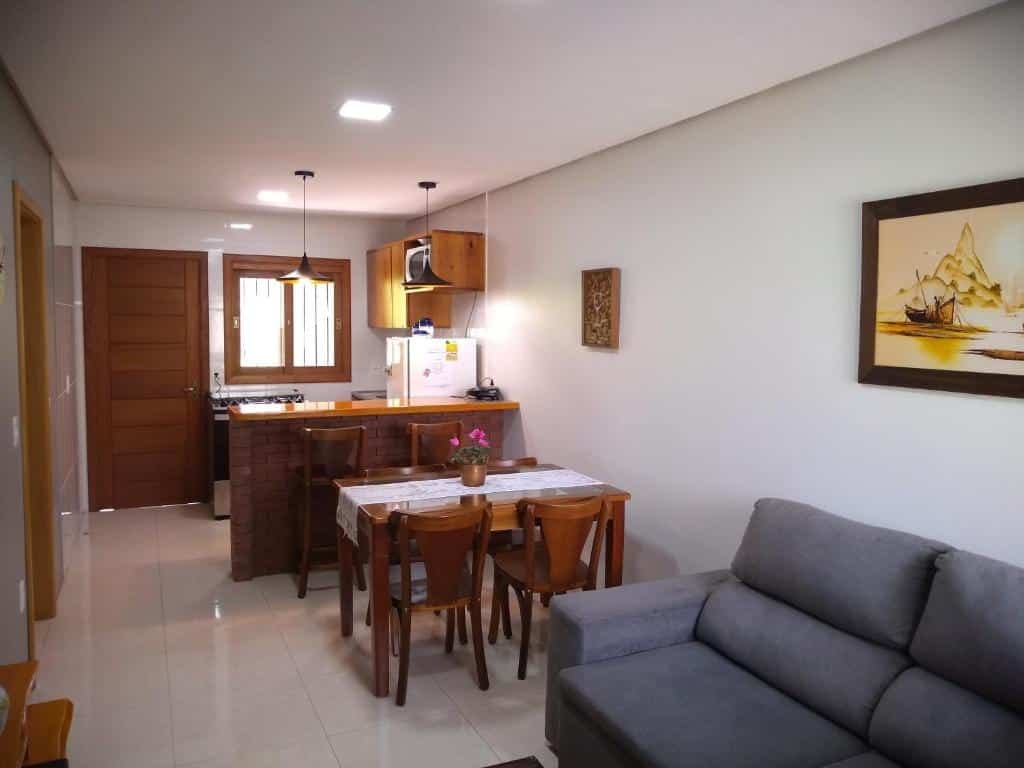 Sala e cozinha do Residencial Franzen. O sofá está no canto inferior direito. A mesa com quatro cadeiras está mais ao fundo, e depois dela, a cozinha equipada com geladeira, armários, pia, fogão e micro-ondas.
