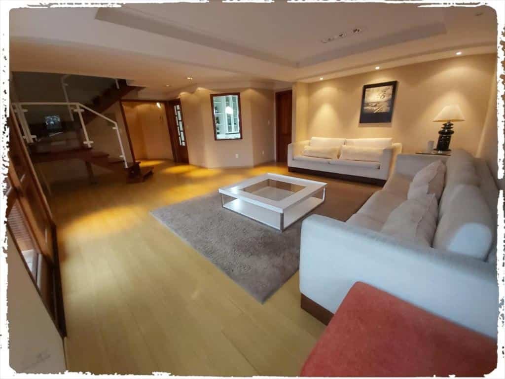 Uma sala espaçosa no Residencial João pessoa. Há dois sofás uma mesa de centro entre eles e um abajur. No fundo à esquerda vemos uma escada que leva ao segundo andar.