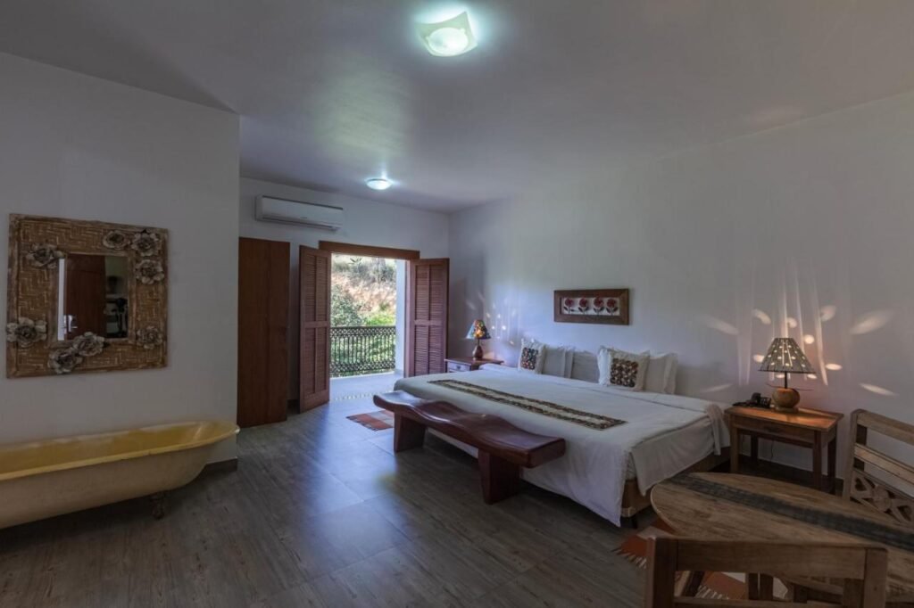 Um quarto do Hotel Fazenda 3 Pinheiros com uma cama de casal, um espelho decorativo, móveis de madeira, uma banheira com pés e uma porta que dá para o lado de fora.