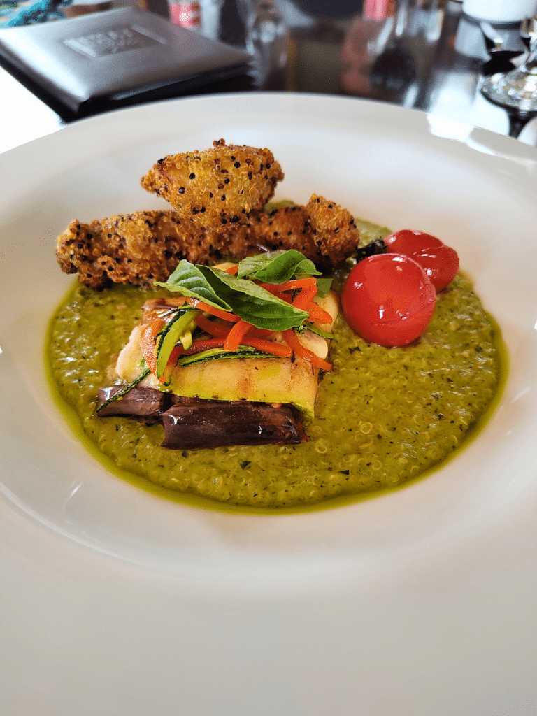 prato arredondado branco com uma sopa de quinoa, legumes assados em cima, acompanhado de tomates cerejas e filés de frango a milanesa