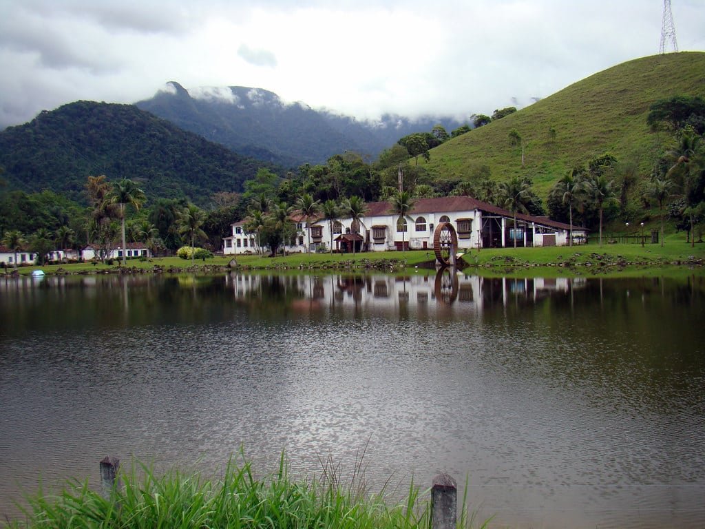 Lago com uma margem gramada, uma casa branca e uma roda d