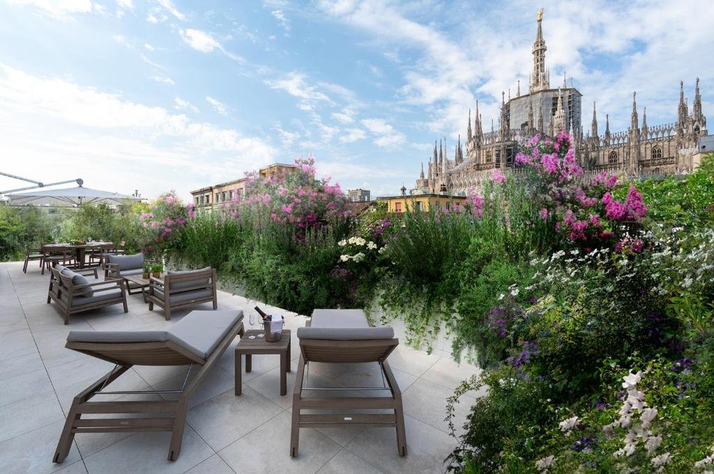 Terraço do Rosa Grand Milano - Starhotels Collezione com vista para a Catedral de Milão cercado por flores, há espreguiçadeiras e bancos com almofadas, para representar hotéis melhores hotéis em Milão