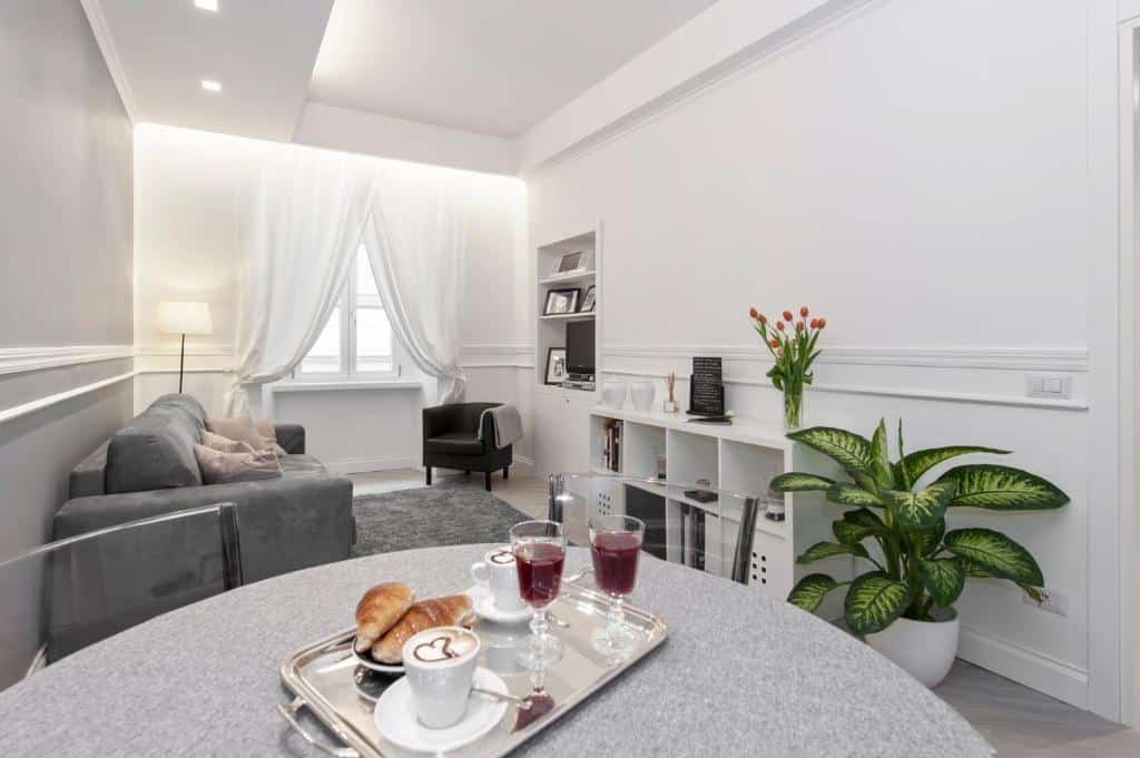 sala do Trevi Apartment, com mesa redonda com cadeiras e café da manhã posto, sofá que vira um sofá-cama, janela grande com cortinas claras e nichos com decoração em frente, além de poltrona