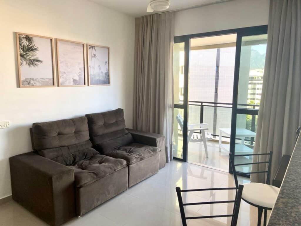 Sala de estar do Apartamento renovado Barra Bella com sofá do lado esquerdo da imagem em frente do sofá duas cadeiras e do lado esquerdo do sofá acesso a varanda.