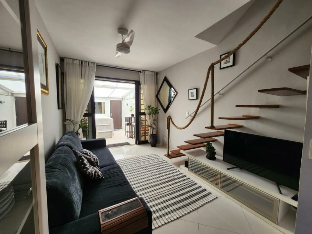 Sala de estar do AP Pepê ALECRIM com JACUZZI e SOLÁRIO Frente ao MAR com sofá do lado esquerdo da imagem com um cômoda com TV em frente.