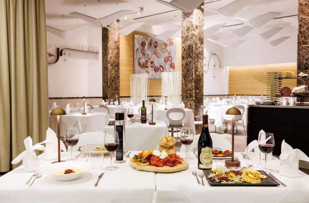 salão do Best Western Premier Hotel Royal Santina com toalhas brancas, cadeiras confortáveis, com quadros na parede e colunas trabalhadas, vinhos e frios estão servidos na mesa