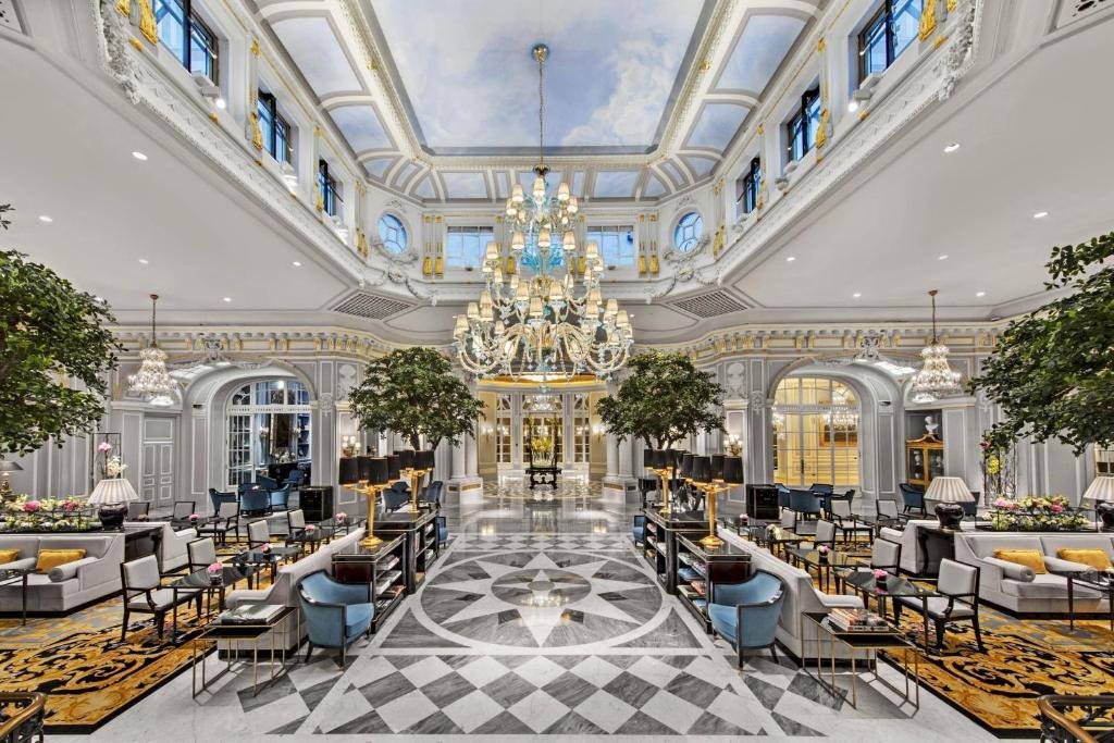 salão do The St. Regis Rome com lustre enorme pendurado em um teto com afrescos e muitas poltronas e mesinhas ao redor