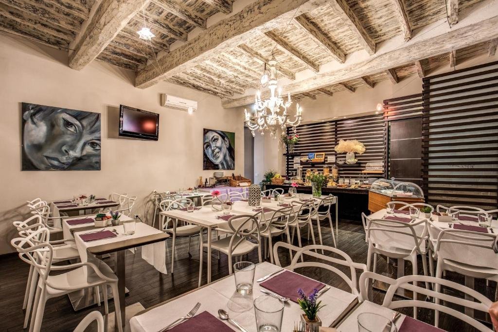 salão do Trevi Beau Boutique Hotel com mesas e cadeiras brancas trabalhadas e confortáveis, há um lustre acima e o teto é todo trabalhado em madeira, os tons são lilás pelo ambiente e há quadros na parede