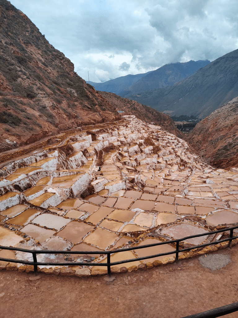 vista panorâmica das salinas de maras, no Vale sagrado dos incas. São várias piscinas de águas salgadas cortadas direto na rocha, mostrando paredes brancas de sal em pedra e águas em tons marrom dentro de cada piscina, que varia de tom a cada uma.