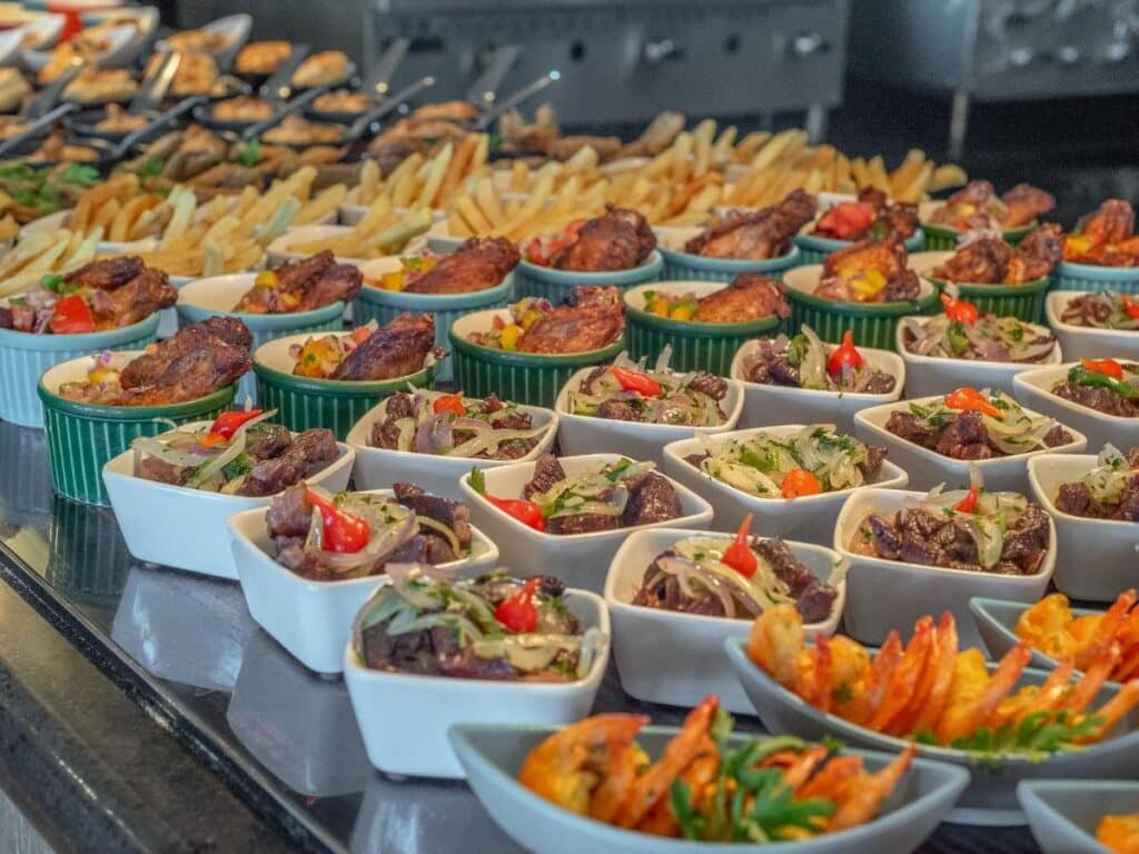 Um bufê com carnes grelhadas variadas, batatas fritas, camarões e pratos coloridos decorados em tigelas brancas quadradas no do Salinas Maceio All Inclusive Resort.