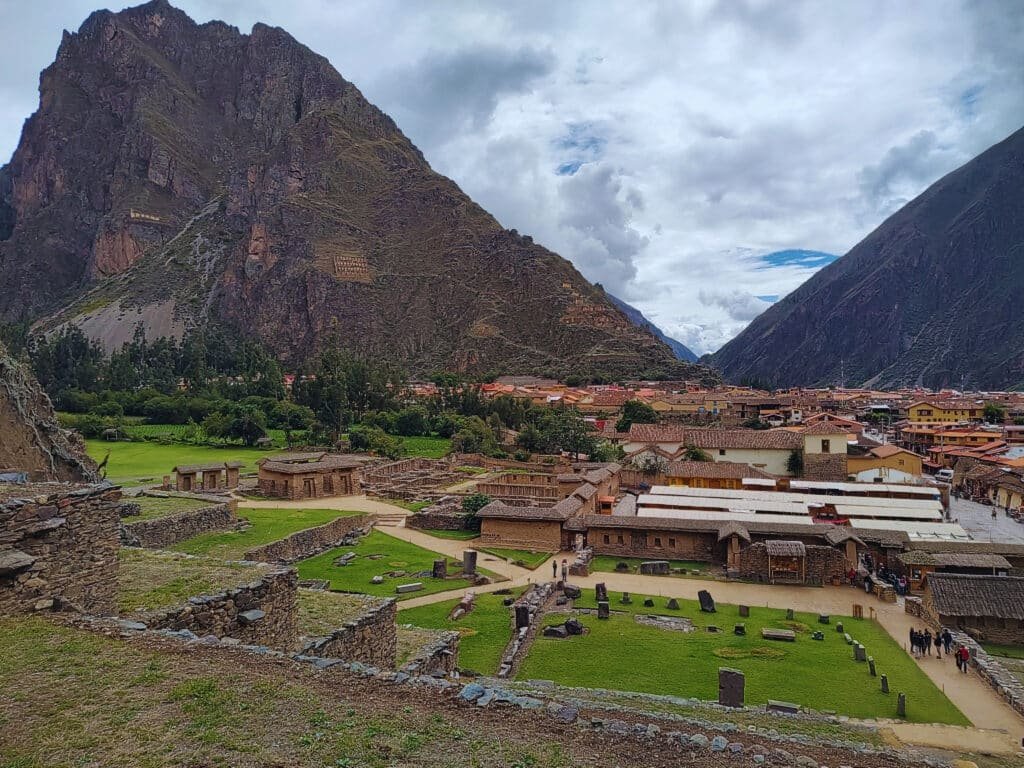vista panorâmica da cidade de Ollantaytambo no Vale Sagrados dos Incas, no Peru. Há uma grande montanha ao fundo, além de um vale repleto de casas antigas e pedras arqueológicas