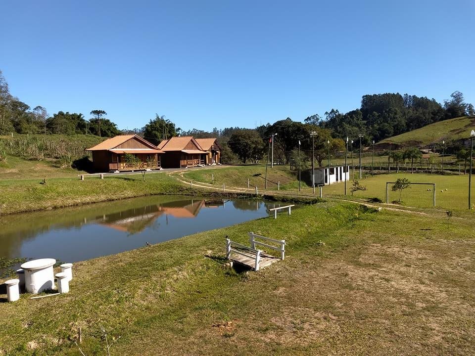 Parte externa do Sitio Esperanca com ampla área de gramado e um lago no meio. Ao fundo estão as acomodações em estilo de chalé.