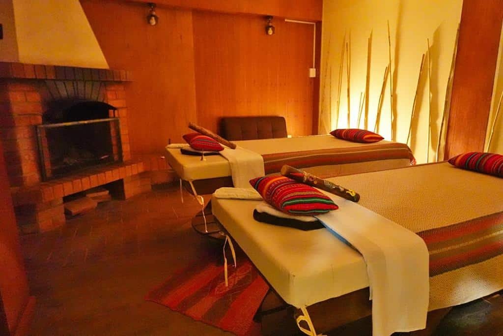 espaço de massagem, spa e relaxamento do Hotel Monasterio San Pedro com duas camas para massagem no lado direito da imagem e uma grande lareira no lado esquerdo.