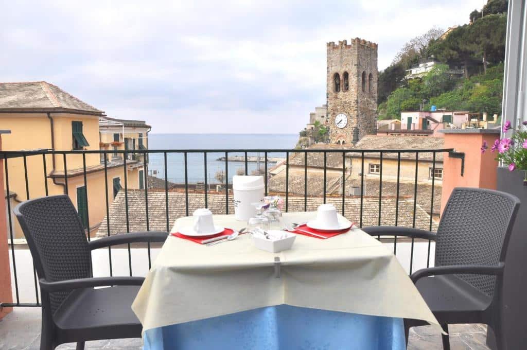 Uma mesa com xícaras e duas cadeiras pretas com vista para as construções, montanha e mar da cidade durante o dia, ilustrando post Hotéis Cinque Terre.