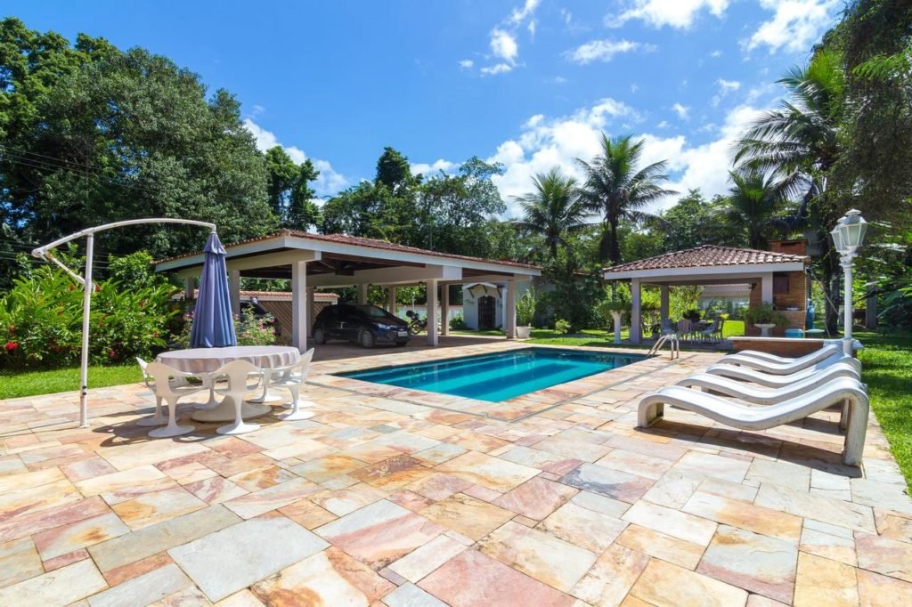 Área externa com piscina e espreguiçadeiras, envolta por verde, na Suites Prime
