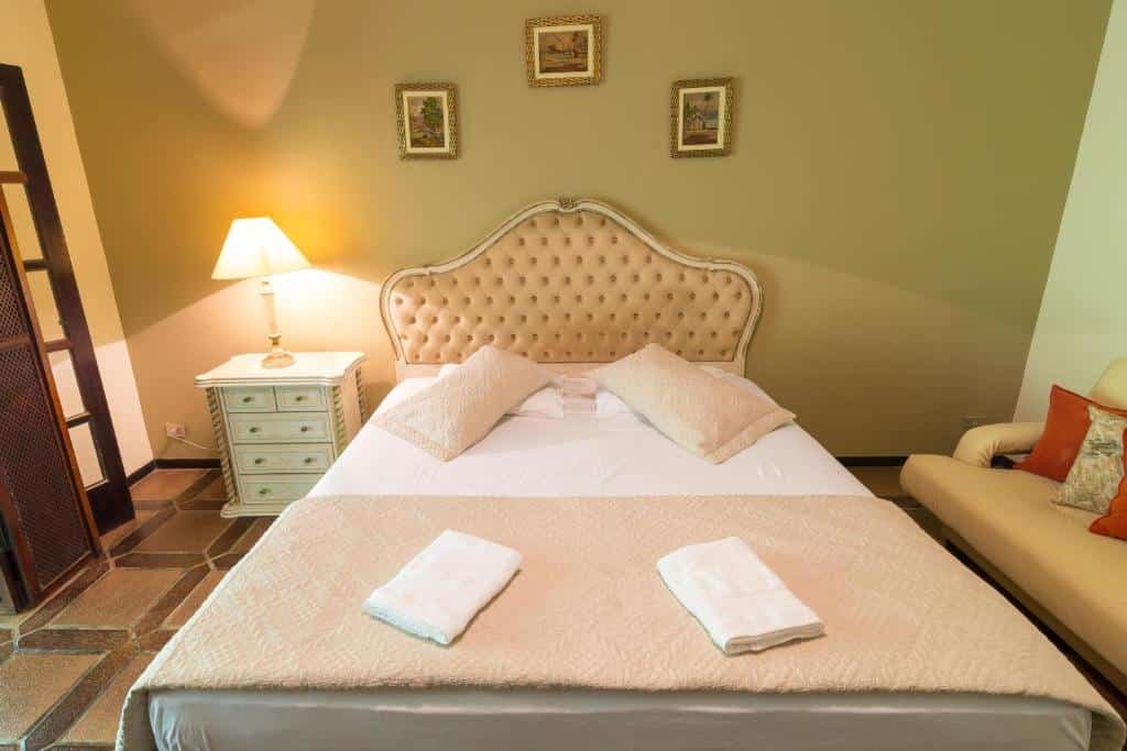 Quarto da Suites Prime. No meio uma cama de casal, no lado direito um sofá, do lado esquerdo uma cômoda com um abajur.