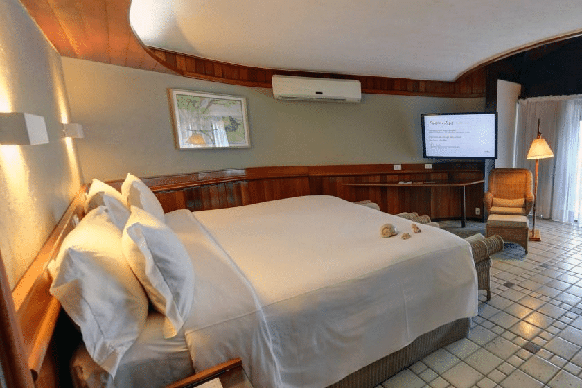 Quarto do Summerville Resort - All Inclusive com uma cama grande, móveis de madeira, arte na parede, TV de tela plana e porta de vidro deslizante com cortina.