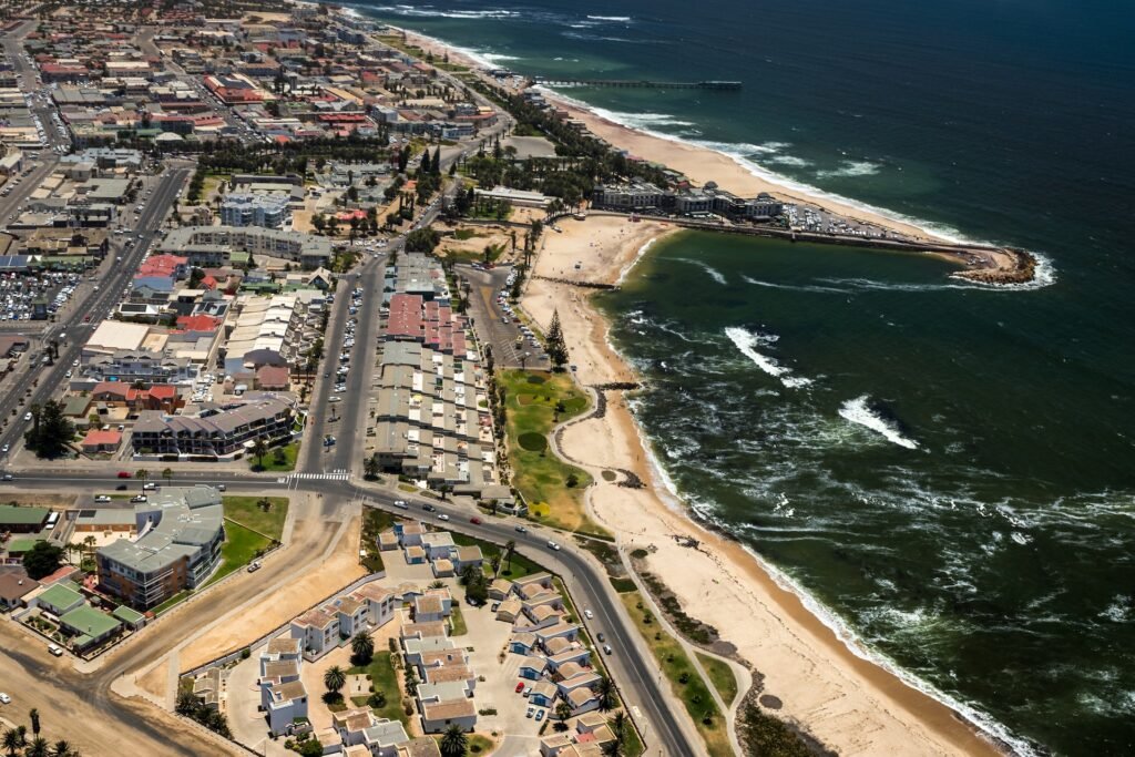 Vista aérea de Swakopmund, cidade na Namíbia, com mar esverdeado e construções (casas, prédios, galpões e etc)